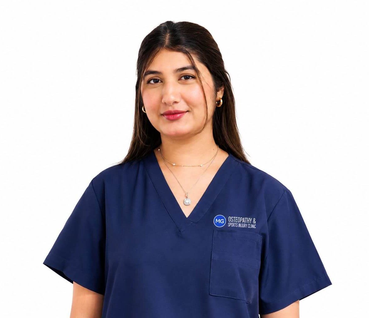 Young woman in navy scrubs with clinic logo on pocket, facing slightly left and smiling.
